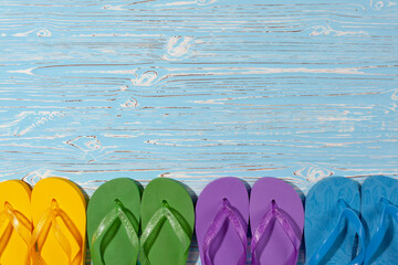 four pairs of multi-colored rubber beach flip flops on a blue wooden background, place under the text