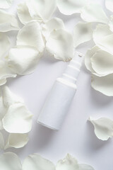 White spray bottle with rose petals on white background. Flat lay, top view.