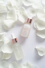Transparent dropper bottles with serum or essential oils and rose petals on white background. Flat lay, top view