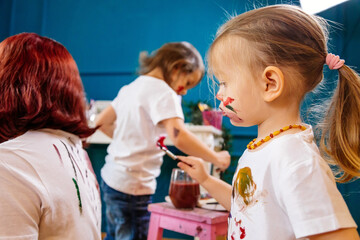 Family hobbies leisure activity home concept. Mother and small daughter drawing with fun using paintbrushes and watercolors. Children and parent creating picture together, body paint, home quarantine