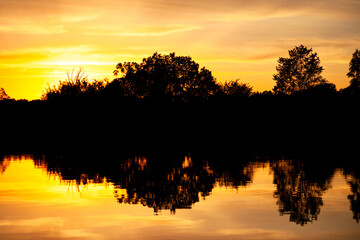 Sunset over the river, silhouette of the forest, mirror image in the water