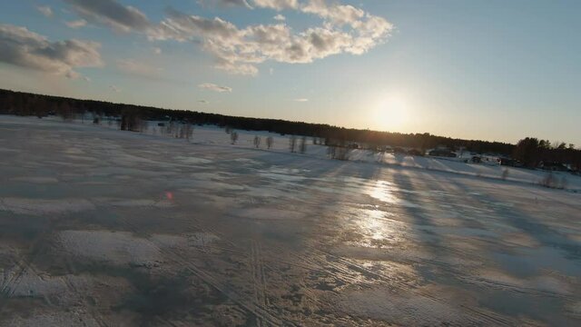 Fascinating speedy video from FPV drone flying to Sunset over melting frozen lake, then turn left, inclined horizon line due fast fly. Northern Sweden, Umea, Stocksjo lake. First person view footage