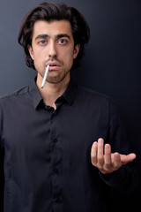 embarrassed man smoking cigarette looking thoughtful and stressed, at a loss. Isolated on black background. Caucasian brunette guy in black shirt look at camera frustrated and confused. copy space