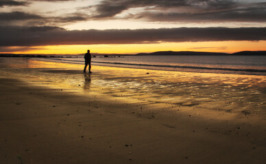 Fototapeta na wymiar Beautiful morning orange sunrise with silhouetted man walking down the beach at Silverstrand, Galway, Ireland 
