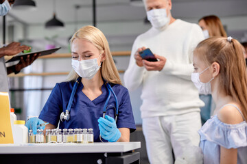 Vaccination against flu or Covid-19 virus. Teenager girl receiving vaccines in modern hospital. Blonde female nurse preparing to give shots to patient child during mass immunization campaign