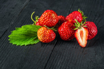 Ripe red strawberries with leaves on a black background. Summer sweet diet and healthy vitamin pack. Free advertising space
