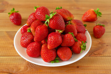 Plate of sweet red strawberries on wooden table. Delicious summer berries.