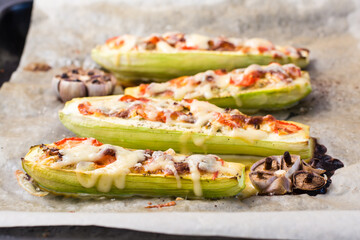 Ready-to-eat baked zucchini halves stuffed with cheese and tomato on baking paper on a baking sheet. Vegetable dishes, healthy food. Close-up