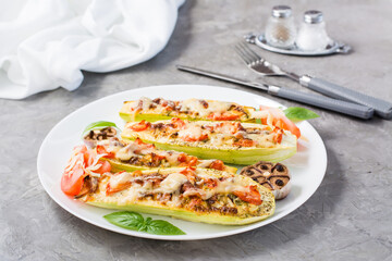 Ready-to-eat baked zucchini halves stuffed with cheese and tomato and basil leaves on a plate on the table. Vegetable dishes, healthy food