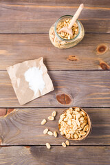 Salted peanuts in a bowl and in a jar with a spoon and salt on paper on a wooden table. Healthy vegetarian food. Rustic style. Vertical and top view