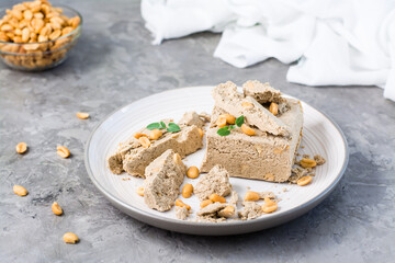 Pieces of sunflower and peanut halva and mint leaves on a plate and a bowl of nuts on the table. Caloric oriental delicacy
