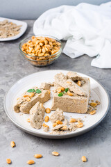 Pieces of sunflower and peanut halva and mint leaves on a plate and a bowl of nuts on the table. Caloric oriental delicacy. Vertical view