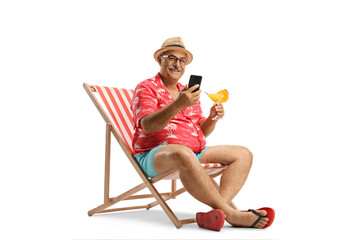 Mature man sitting on a beach chair with a smartphone and a cocktail