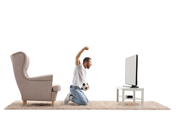Excited man kneeling in front of tv watching a football and cheering