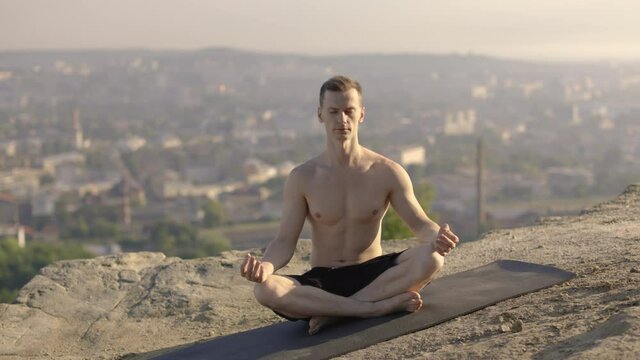 Peaceful shirtless man sitting on yoga mat and practicing lotus pose with closed eyes. Concept of people, sport activity and nature, mindfullness