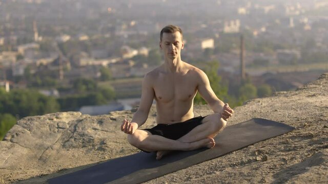 Peaceful relaxed shirtless man sitting on yoga mat in lotus asana and practicing yoga and mindfullness techniques with eyes closed. Concept of people, sport activity and nature.
