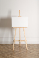Wooden easel with blank canvas near light wall