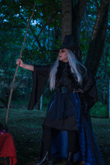 Naklejka premium Woman in a witch costume in the forest at twilight holding a wooden stick