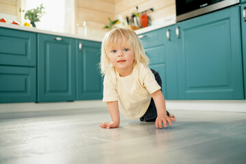 Beautiful little baby blonde boy of European appearance playing on the kitchen floor. Happy...