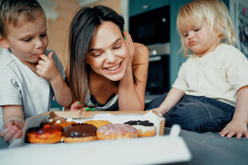 Young family mom and two children boys. Eat sweet dessert donuts pastries. Play fun games in the...