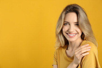 Fototapeta premium Portrait of happy young woman with beautiful blonde hair and charming smile on yellow background. Space for text