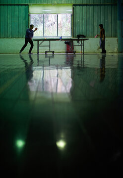 Asian couple playing big table tennis in a special green-toned gymnasium