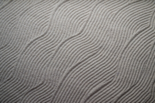 Simple graphic wave patterns raked into a background in the white sand of a Japanese Zen garden