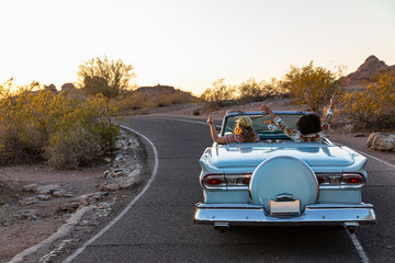 Two Friends driving down road in blue convertible 