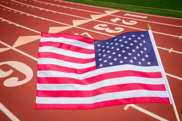 American flag flying over the numbered lanes of the start line of an athletic running track