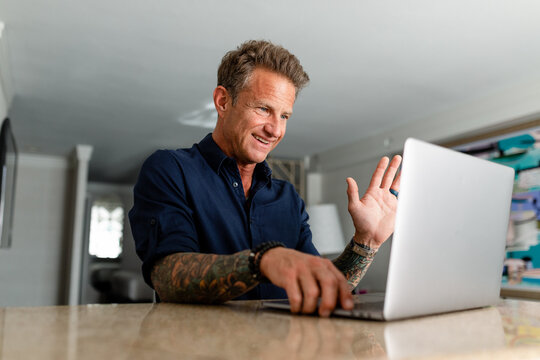 Man Waves Hello in Front of Laptop