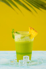 Vertical de un delicioso Jugo de piña con yerba buena en un vaso plástico orgánico en un fondo amarillo