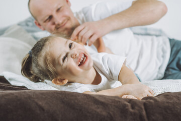 Father plays with little daughter 2-4 on bed. Dad tickles kids feet. Family, having fun
