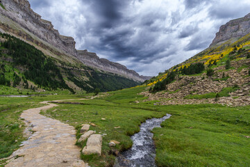 Hiking trail with small mountain creek under rain clouds in the spanish national park Ordesa y Monte Perdido, Pyrenees, Spain - obrazy, fototapety, plakaty