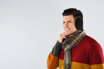 Man wearing stylish earmuffs and scarf on light background. Space for text