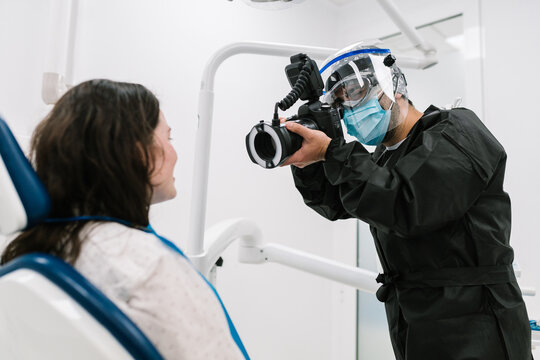 Dentist with mask and protective clothing, taking a photo of his patient.