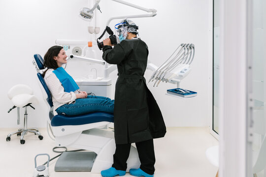 Dentist with mask and protective clothing, taking a photo of his patient.