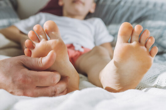 Dad tickles feet of kid. Boy lies on bed and plays with his father. Family, having fun at home
