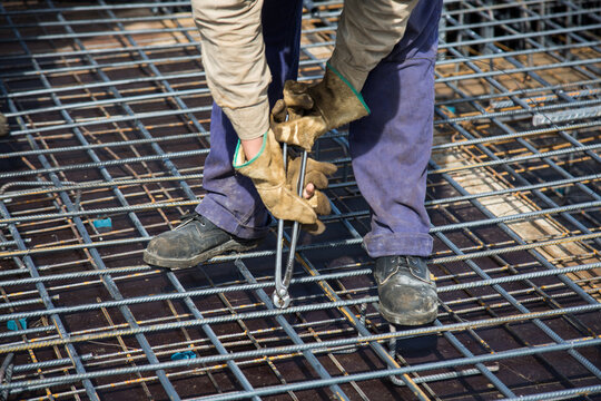 Worker knitting metal rods bars into framework reinforcement