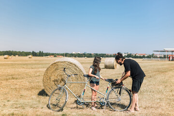 Father and daughter park a tandem bike on the field