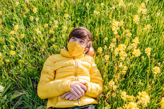 Dreamy teenager in mask lying amidst grass and flowers