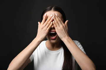 Young woman feeling fear on black background