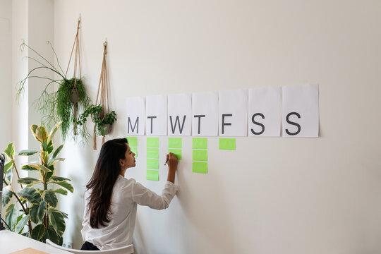 Woman Writing In A Weekly Wall Organizer At Cool Office