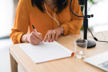 Crop woman recording podcast and taking notes in notebook