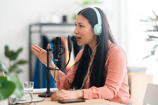 Asian woman in headphones recording podcast in modern studio
