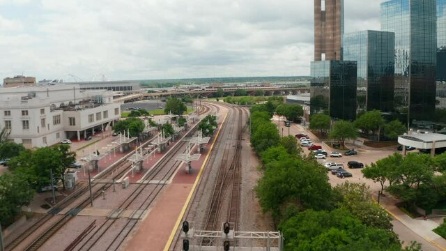 Forwards fly above empty railway tracks in station. Group of tall modern building with glass facade on side. Dallas, Texas, US.