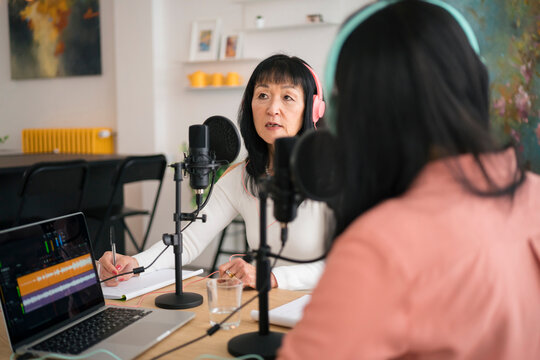 Asian woman speaking to microphone during podcast recording with colleague