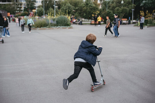 A little boy rides a scooter in the park.