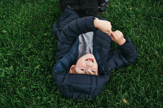 A little boy is lying on the green grass.
