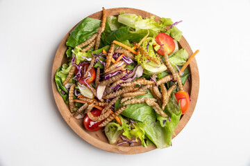 Vegetable salad with fried bamboo caterpillar in a wooden bowl.