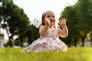 One small caucasian baby girl sitting on the grass wearing dress in the field in summer or autumn...